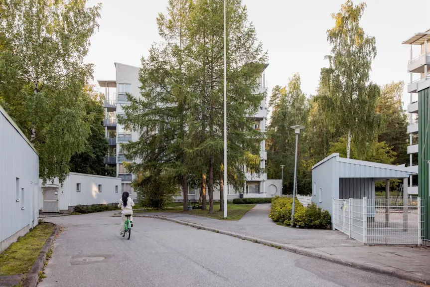 Tyttö pyöräilee vaaleiden kerrostalojen välissä. 
