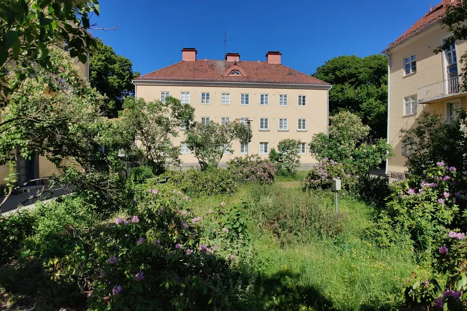 Vehreä sisäpihakortteli. Korttelissa kolme kolmekerroksista vaaleaa kerrostaloa.