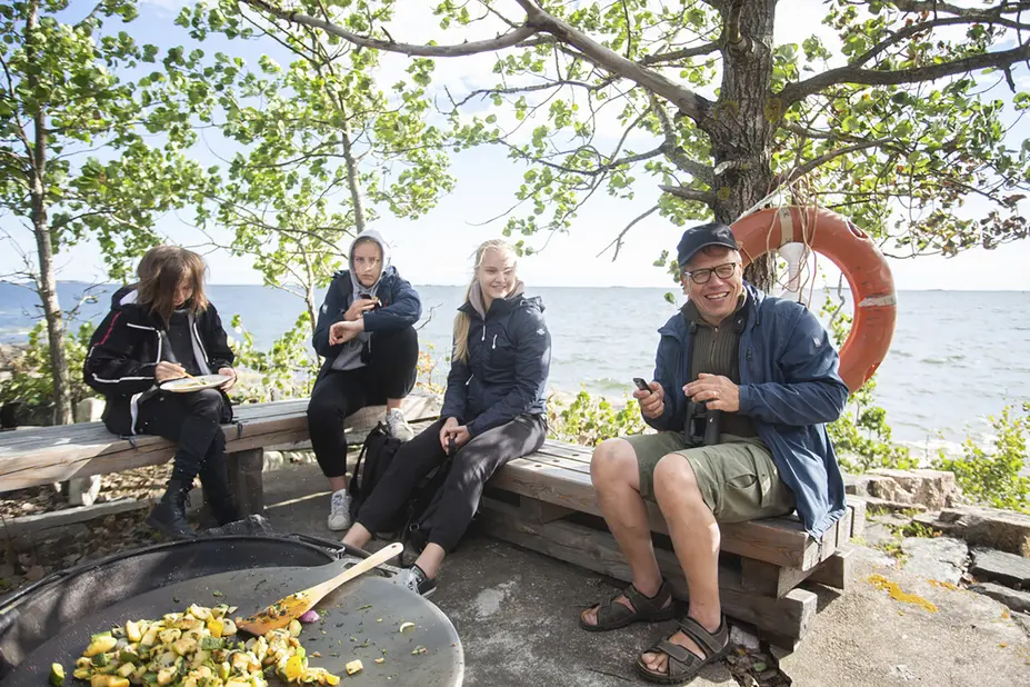 Ihmisiä istuu penkeillä merimaiseman äärellä