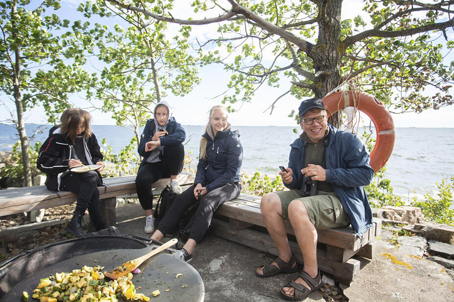 Ihmisiä istuu penkeillä merimaiseman äärellä