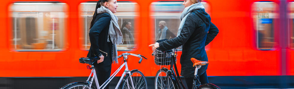 Kaksi pyöräilijää odottaa metroa metroaseman laiturilla.