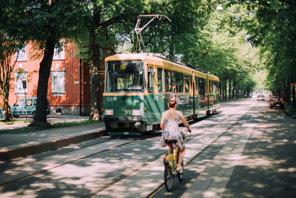 Nainen pyöräilee vehreällä kadulla ja vastaan tulee raitiovaunu.