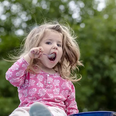 En liten flicka äter en parkmåltid sommaren 2021.
