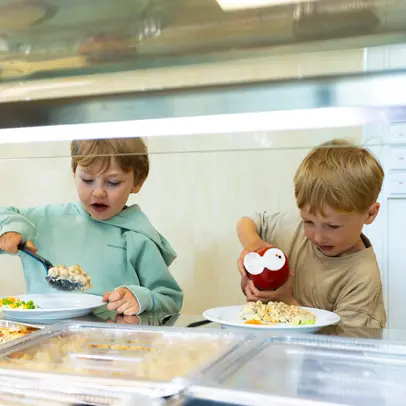 Två barn på dagis som tar mat från serveringslinjen."