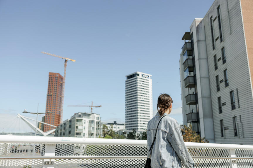 Henkilö kävelee sillalla ja katselee valmiita sekä rakenteilla olevia kerrostaloja.