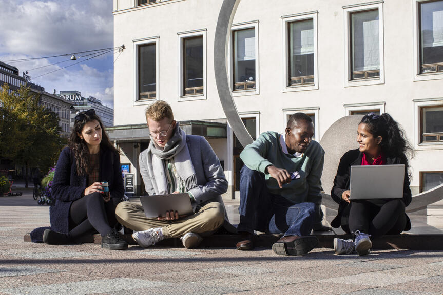 Four people sit outside and work with laptops.