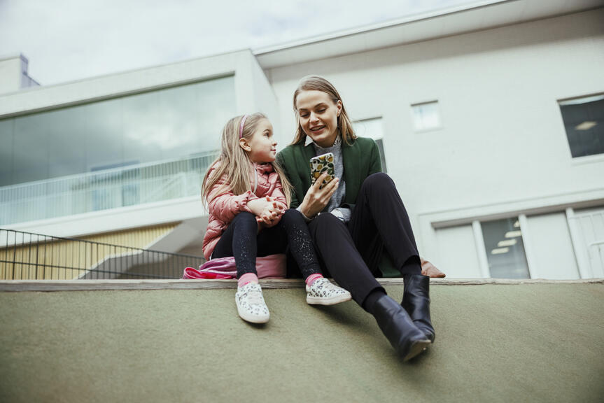 Ett barn och en kvinna sitter utanför och tittar på en smartphone.
