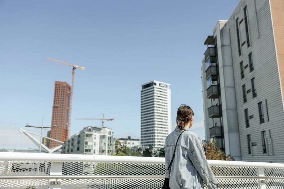 Henkilö kävelee sillalla ja katselee valmiita sekä rakenteilla olevia kerrostaloja.