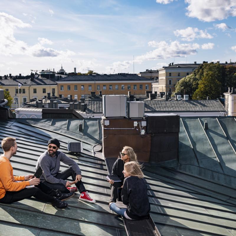 Neljä ihmistä istumassa ja keskustelemassa talon katolla.