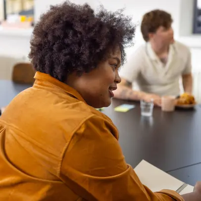 A woman with a pen and paper at a table, with other people in the background.