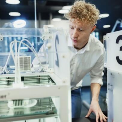 A young man uses a 3D printer in a library.