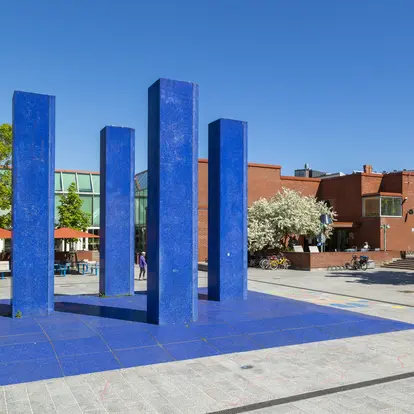 Four large blue columns in front of a low brick building. 