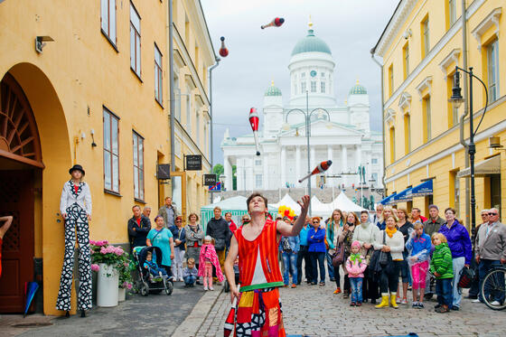 An audience watching a juggler's tricks in the Helsinki market quarters.