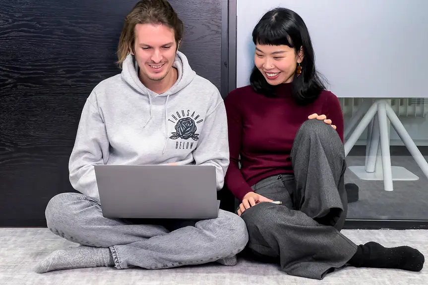 Two people are sitting on the floor and looking at a laptop.