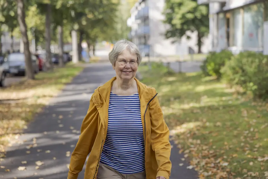 A smiling senior walks on the pavement among the trees.