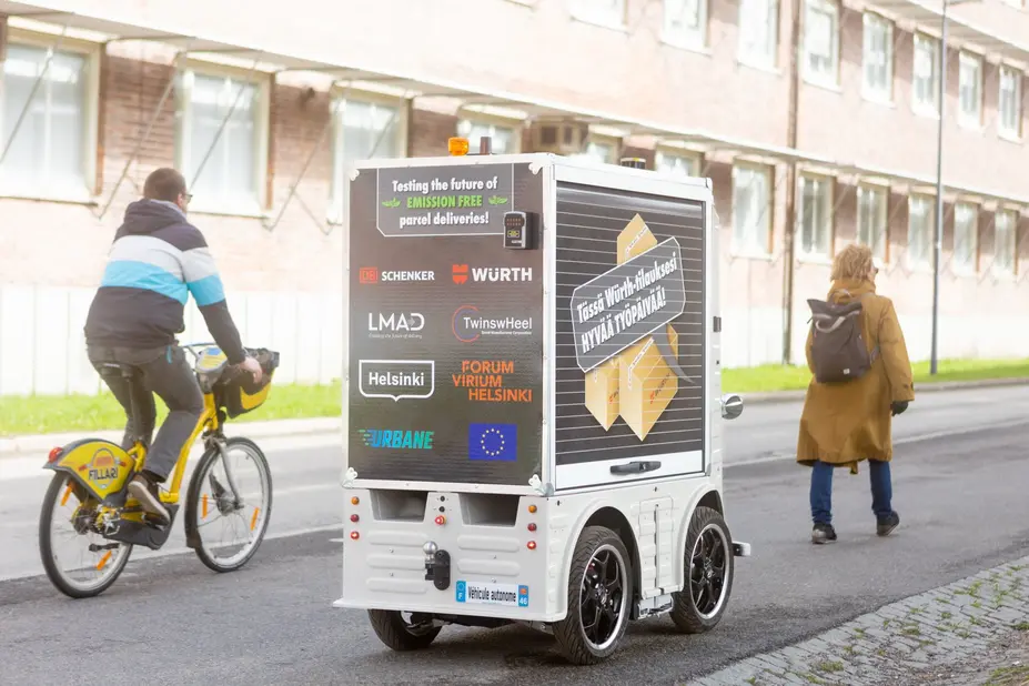 Pyöräilijä, jalankulkija ja pieni robottibussi kadulla.