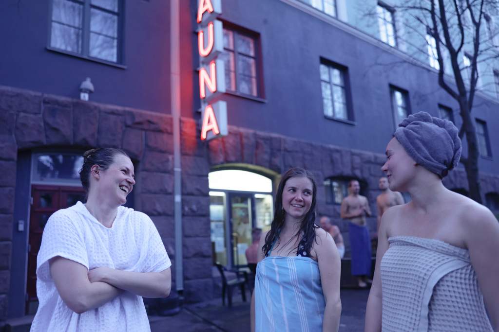Kolme naista julkisen saunan edessä saunomisen lomassa
