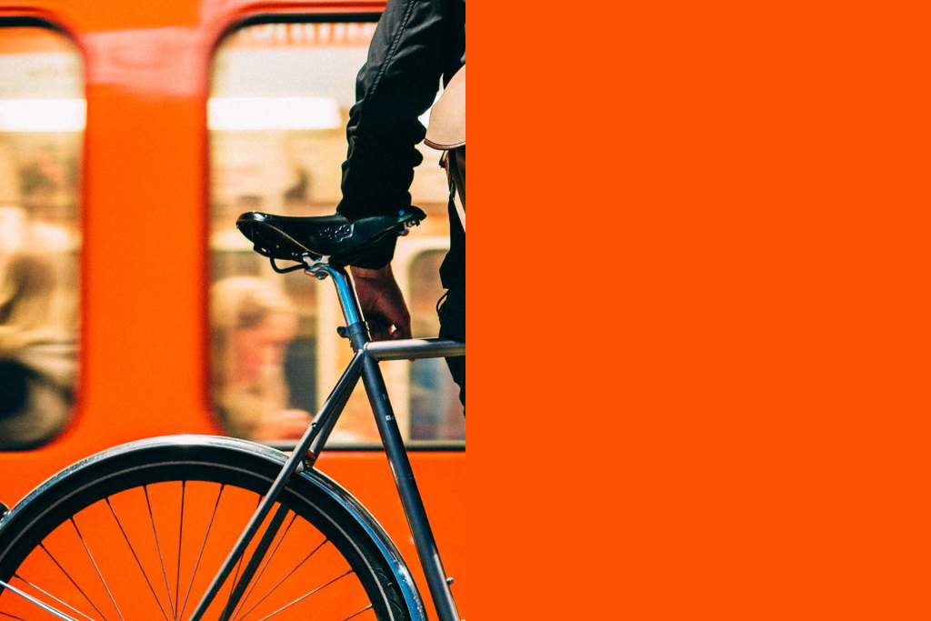 Henkilö seissoo pyörän kanssa oranssinvärisen metron edessä.
