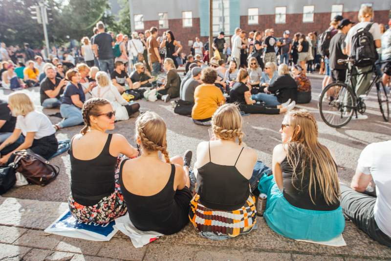 Four young women sit on the ground  in a festival area in Kallio district.