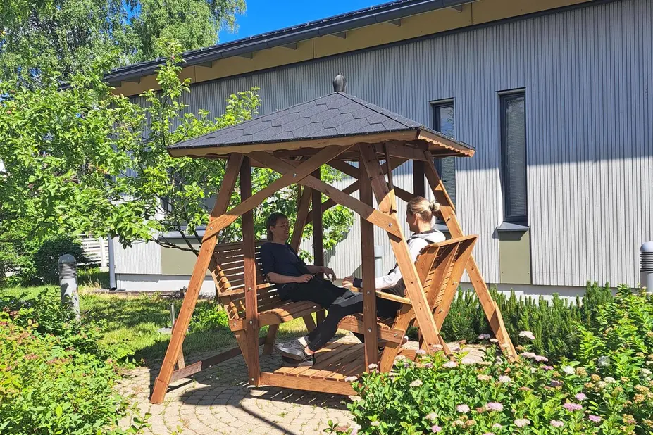 Two people are sitting on a swing in a summer yard.
