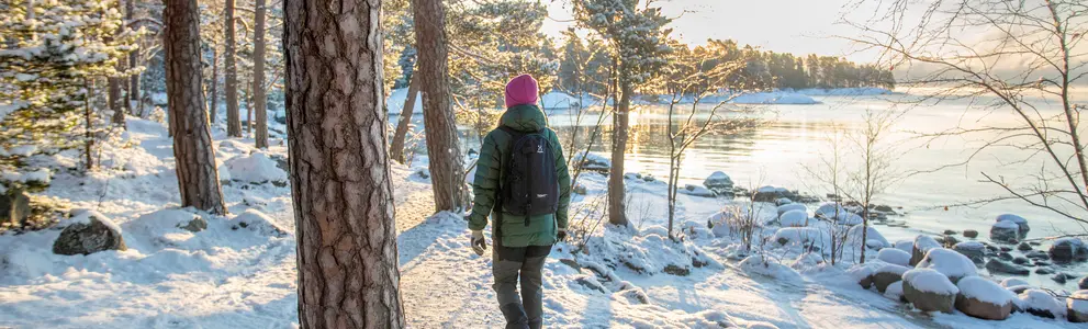 Nainen kävelee talvisessa metsässä järven rannalla.